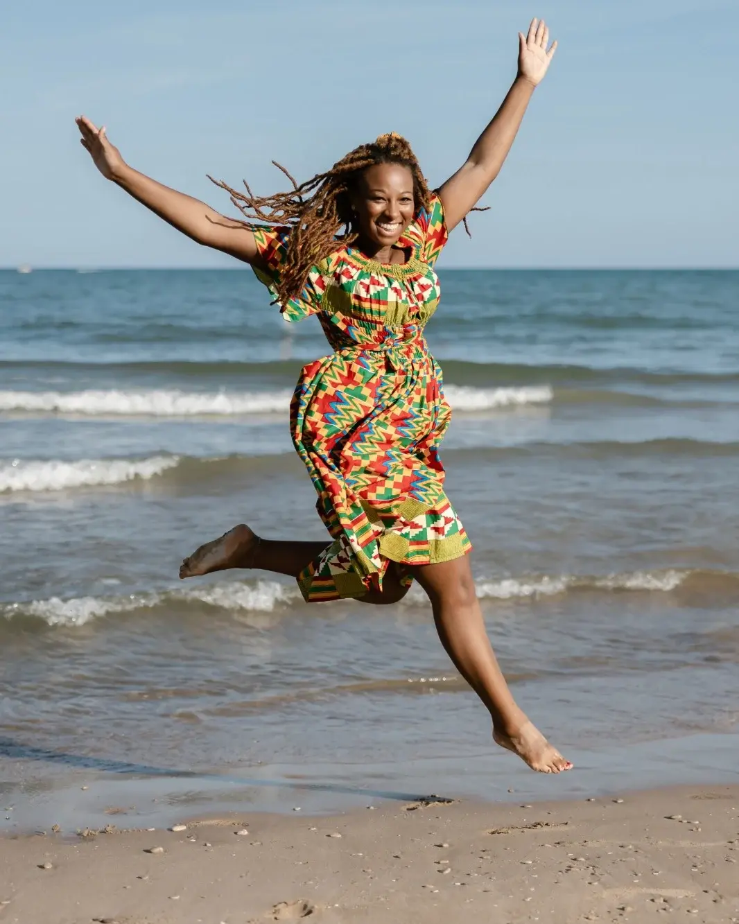 Lakisha, Gründerin von Kofferfreundin, springt lachend am Strand in die Luft